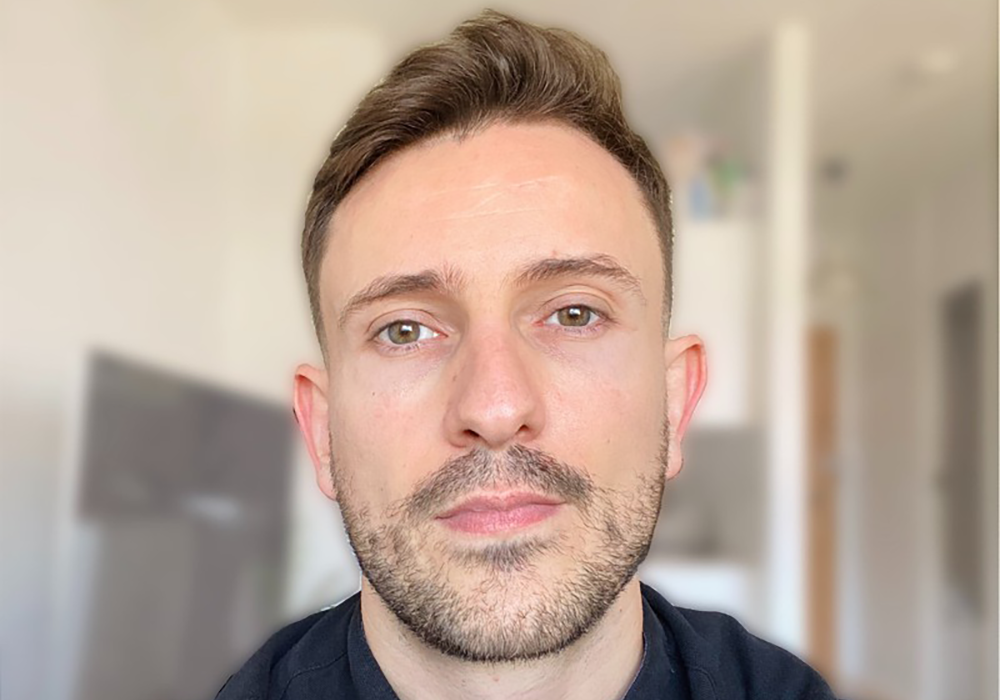 Photo of Tyler Huntley. He has short brown hair, and has a beard. He is looking at the camera with a blurred background.