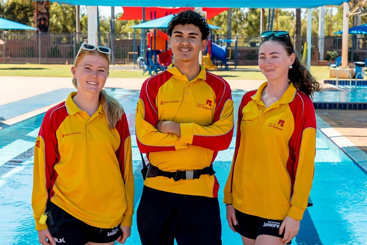 Three young lifesavers standing in their work clothes in front of a pool in port headland