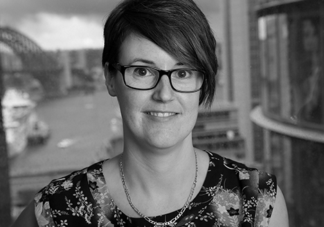 Photo of a woman with short hair, glasses and wearing a necklace. She is smiling at the camera.