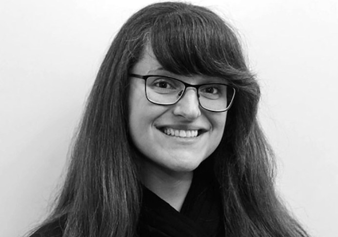 Photo of a woman with long dark hair, wearing glasses. She is smiling at the camera.