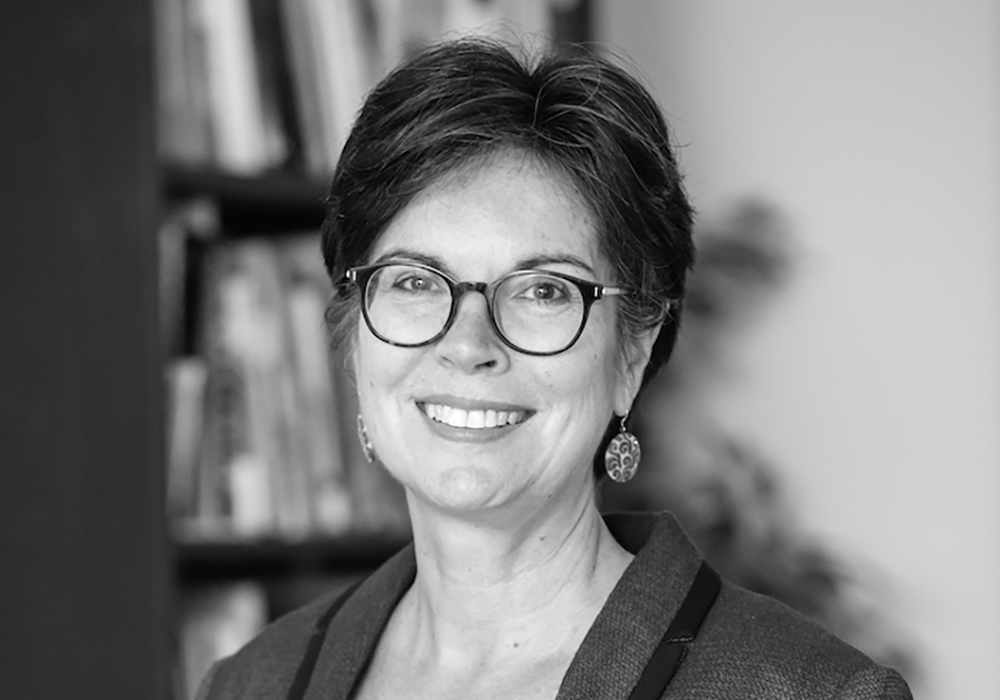 Photo of a woman with short dark hair, wearing glasses and earrings. She is smiling at the camera.