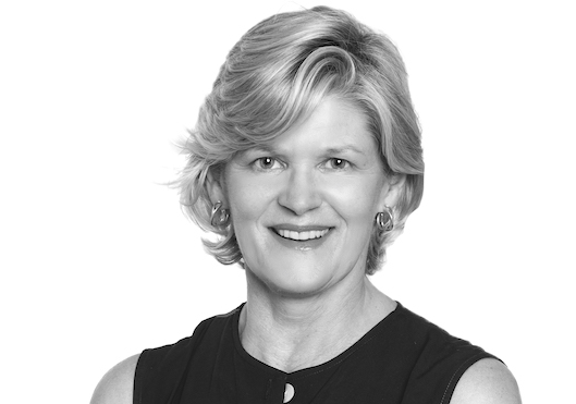 Photo of a woman with short light hair, wearing a black top and earrings. She is smiling at the camera.