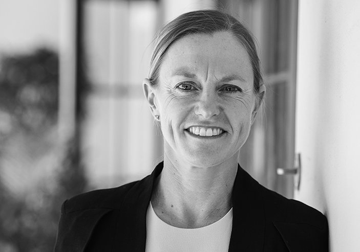 Photo of a woman with hair tied back, wearing a white top and black blazer. She is smiling at the camera.