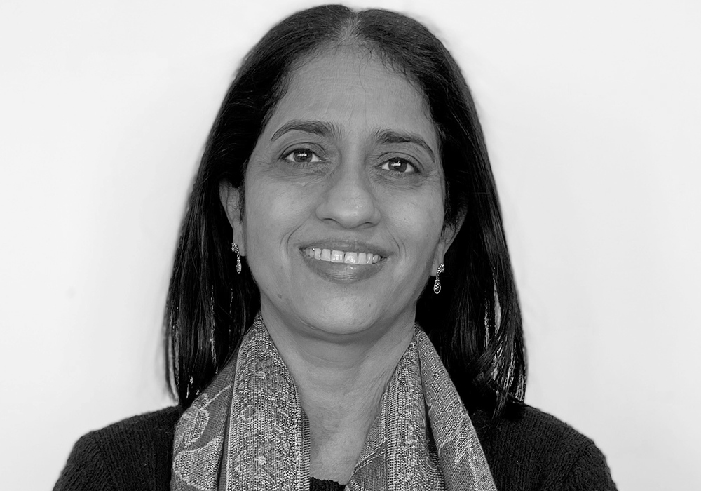 Photo of a woman with long dark hair, wearing a scarf. She is smiling at the camera.