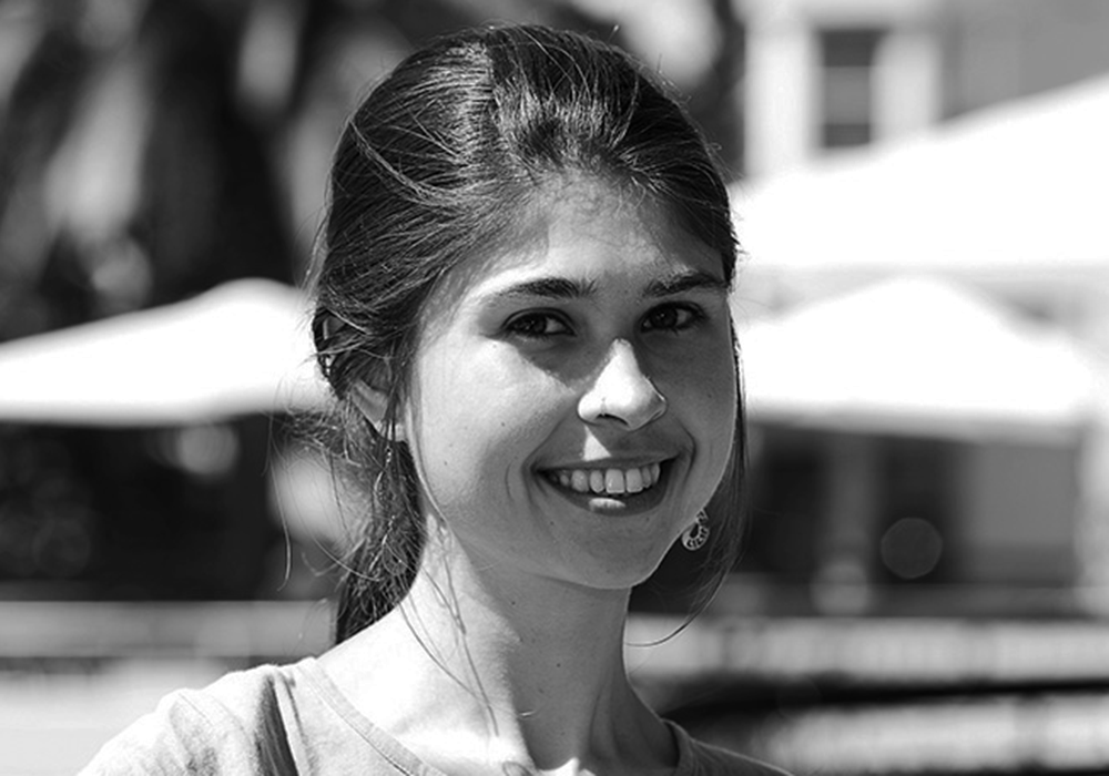 Photo of a woman with long hair tied back into a ponytail. She is smiling at the camera.