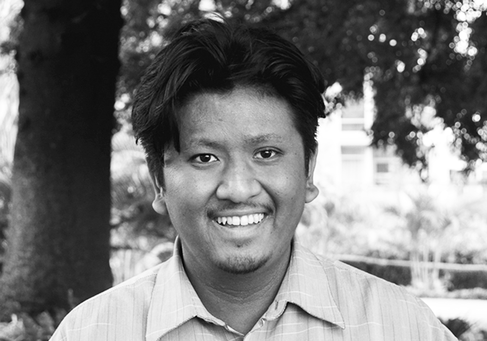 Photo of a man with black hair and a light collared shirt. He is smiling at the camera.