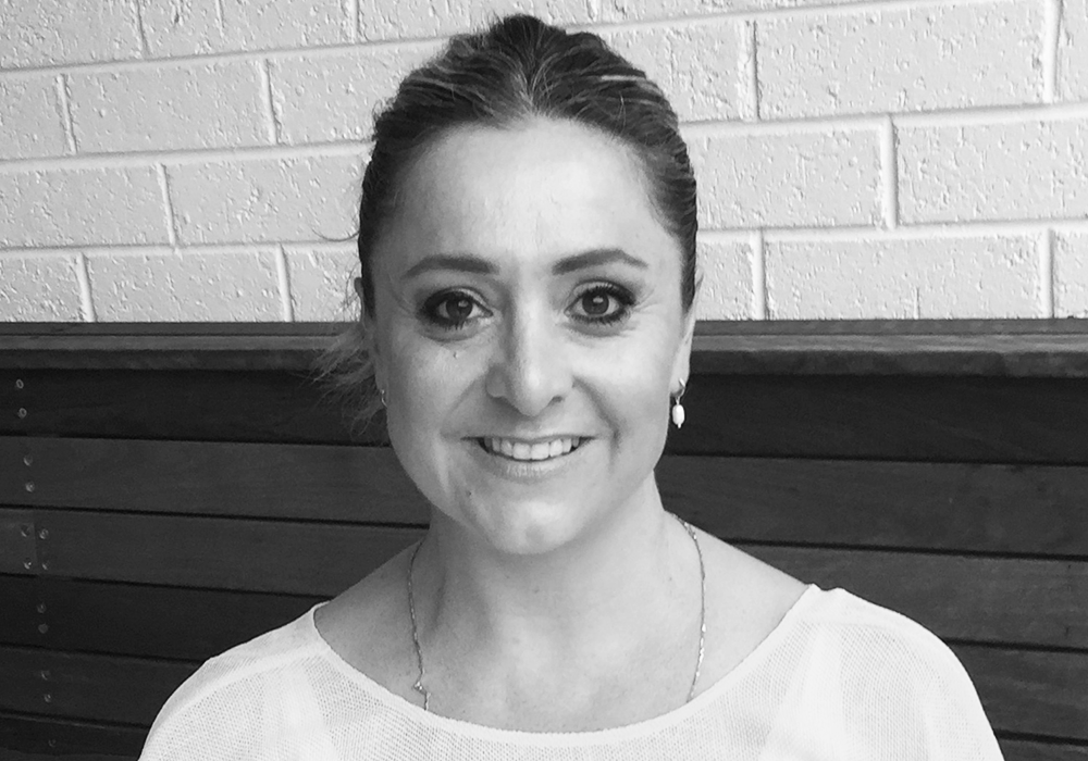 Photo of a woman with dark hair tied back. She is smiling at the camera.